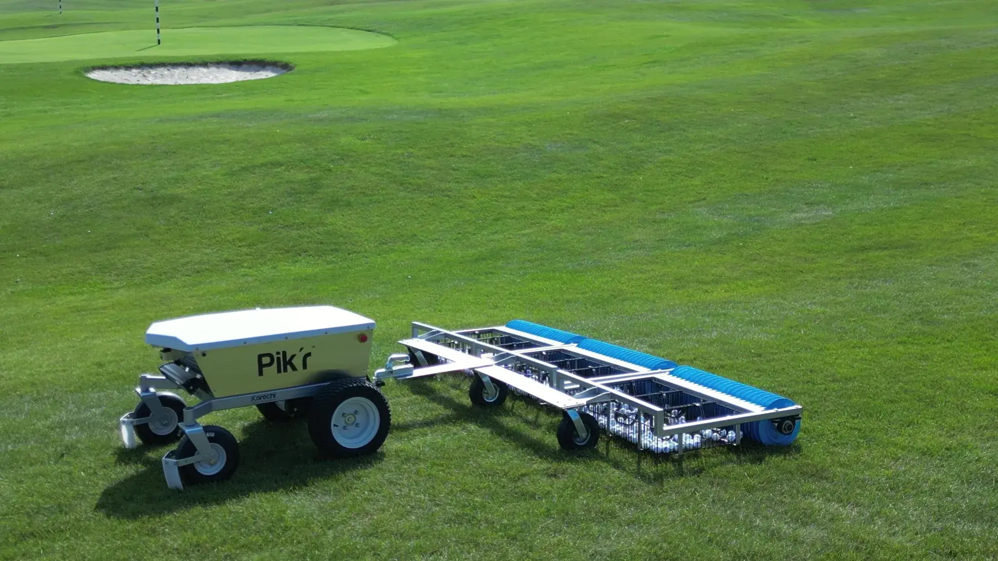 A Korechi Pik'r-X autonomous range picker towing three picking gangs across a golf course, a bunker and green behind