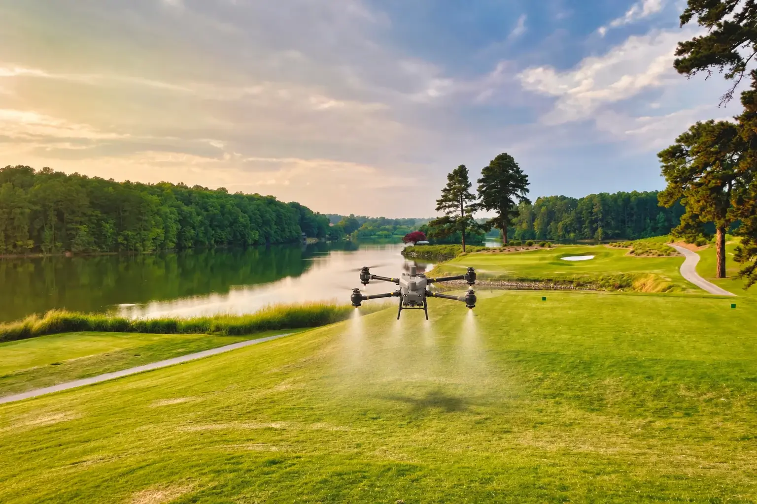 A DJI Agras spray drone flying low over a golf fairway, misting the turf beside a lake