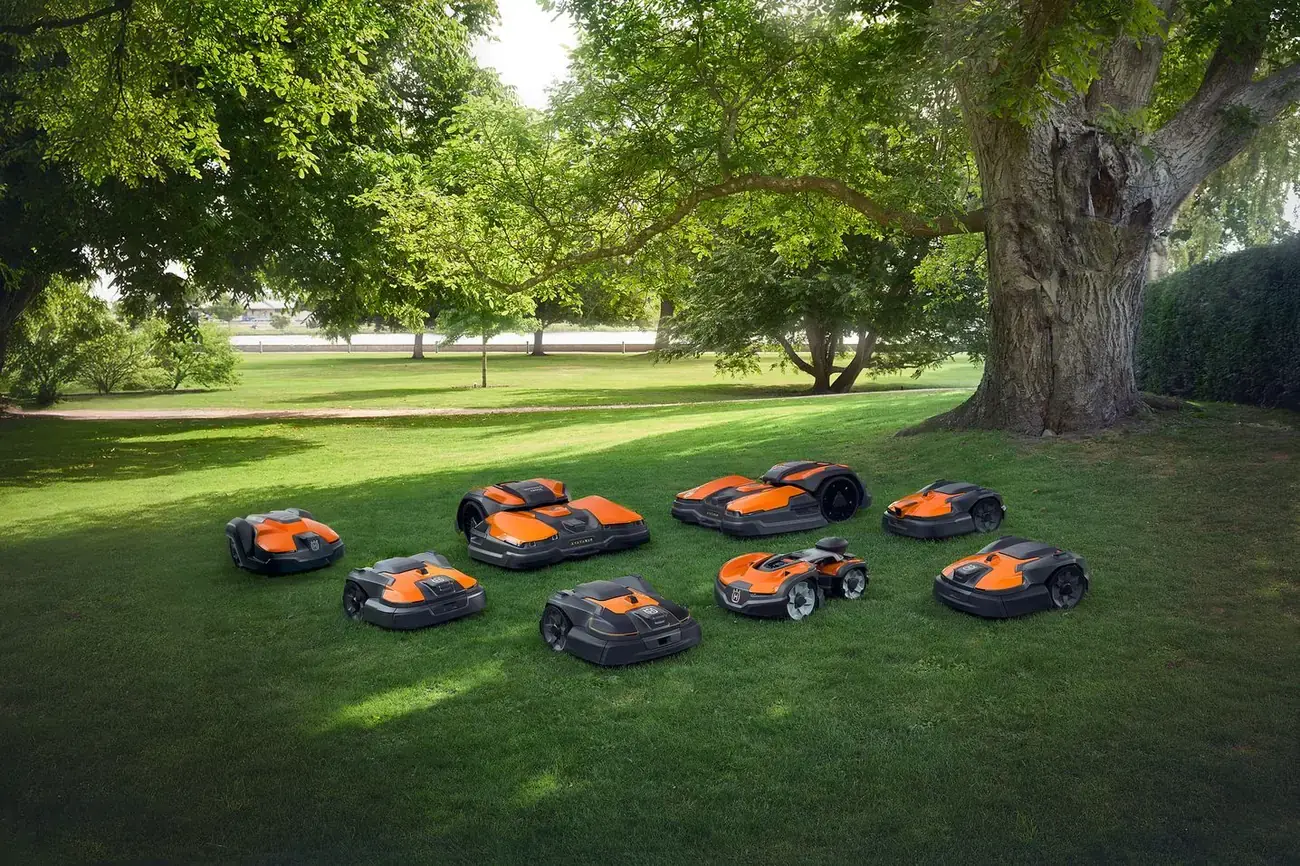 Nine Husqvarna robotic mowers parked together on a lawn under a large oak