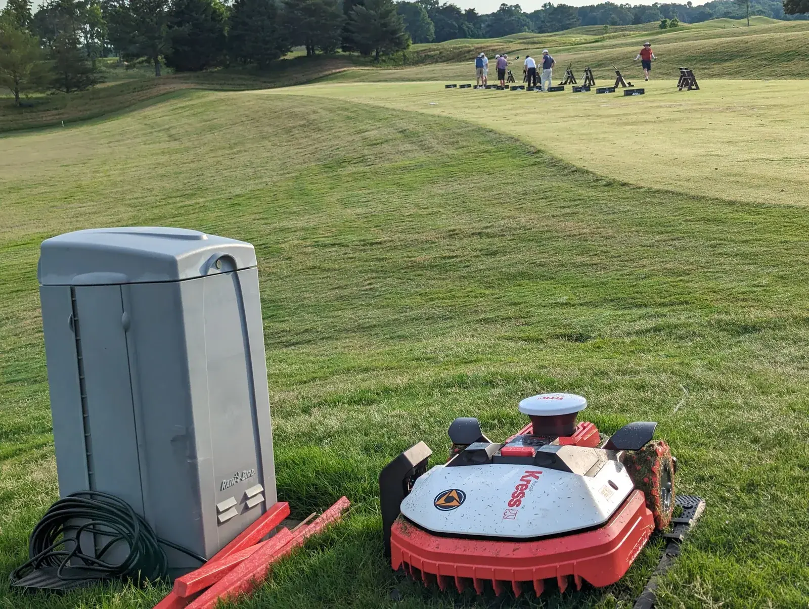 A Kress robotic mower and its charging station beside a busy driving range