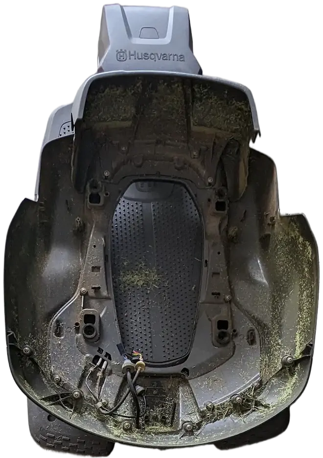The shell of a Husqvarna robotic mower, taken off and turned over, with grass clippings packed along its inside edges