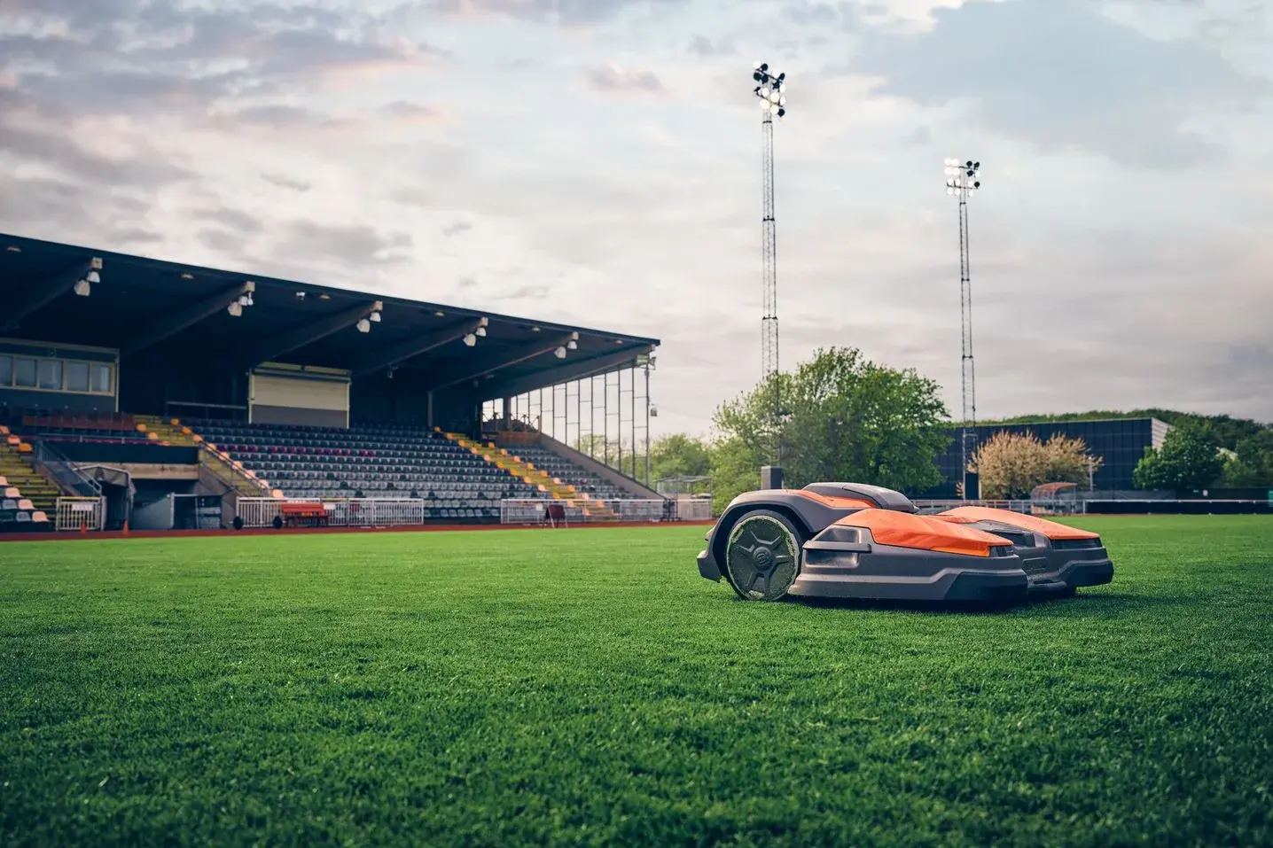 A Husqvarna CEORA robotic mower on a stadium pitch, the stands and floodlights behind it