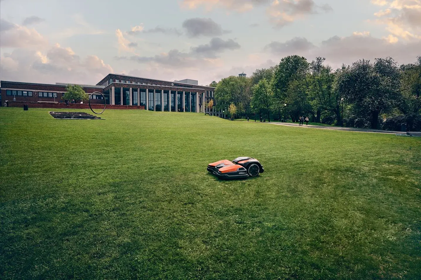 A Husqvarna robotic mower working a broad lawn in front of a low modern office building