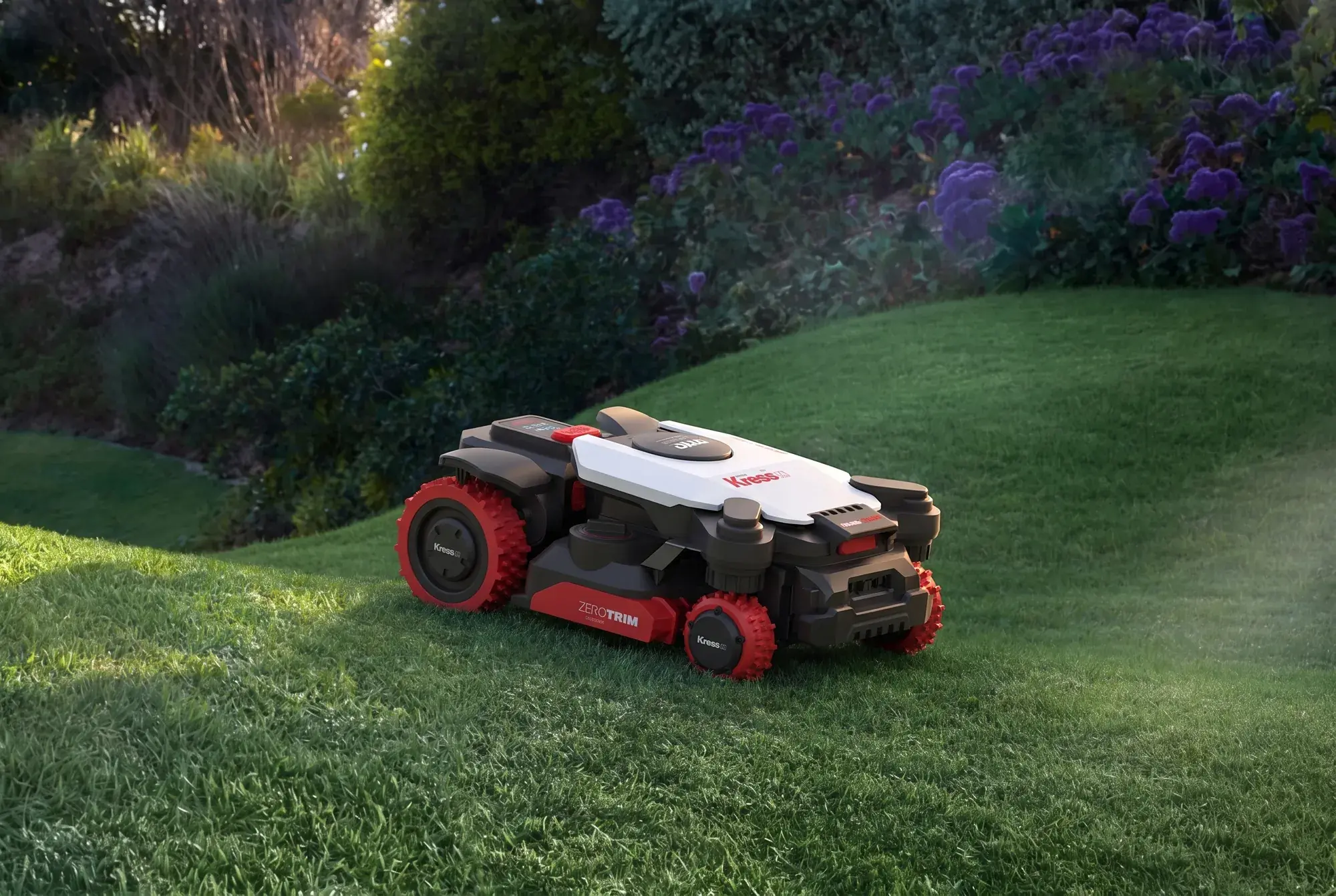 A Kress EyePilot 4x4 robotic mower working a steep garden bank below flowering shrubs