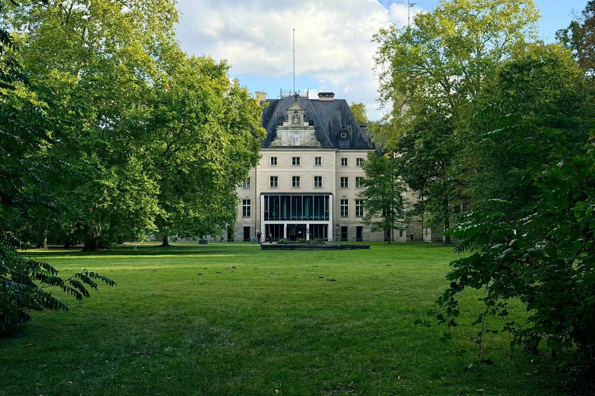 A grand house framed by mature trees above an empty, freshly mown lawn